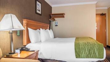 A hotel room with a bed, a bedside table with a lamp, a chair, and a door in the background.
