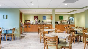 A restaurant with wooden tables and chairs, a counter with coffee machines, and a refrigerator. - Comfort Inn Brockville (Brockville)