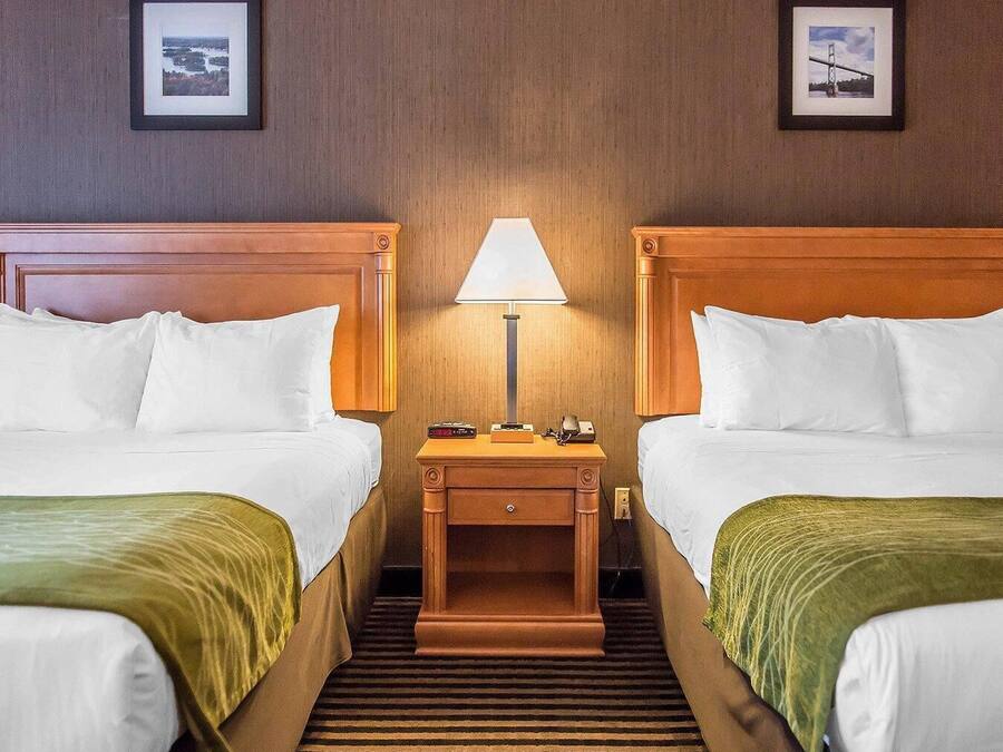 A hotel room with two beds, a nightstand with a lamp, and two framed pictures on the wall.