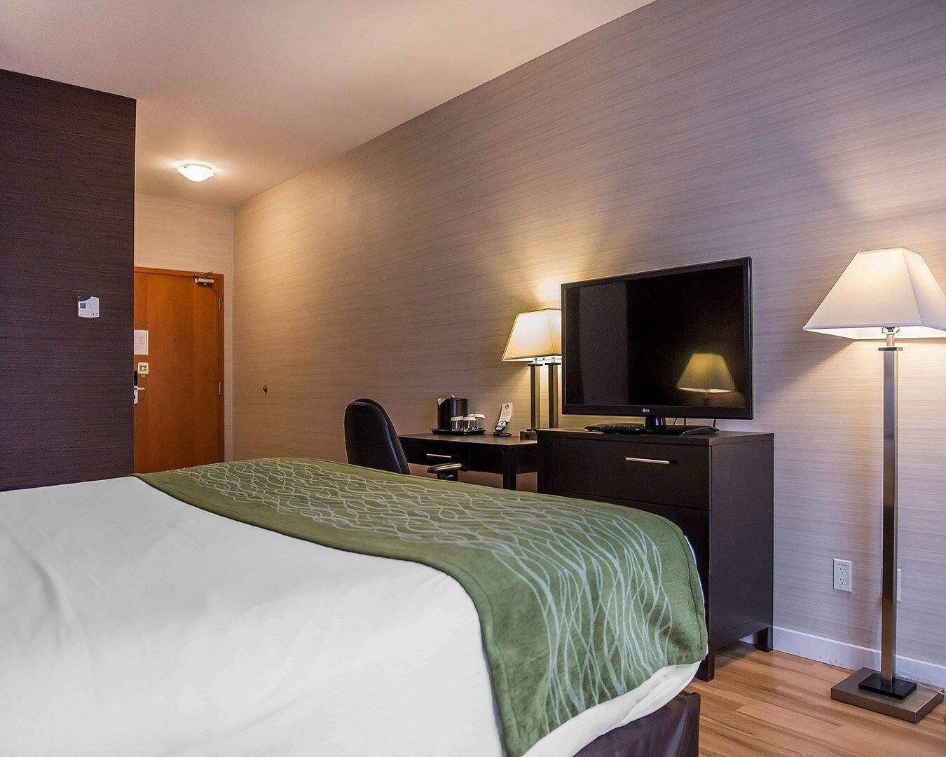 A hotel room with a bed, desk, chair, television, and lamps.