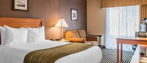 Una habitación de hotel con una cama grande, un escritorio, una silla, una lámpara y una ventana con cortinas.