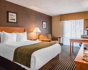 A hotel room with a large bed, a desk, a chair, a lamp, and a window with curtains. - Comfort Inn Brockville (Brockville)