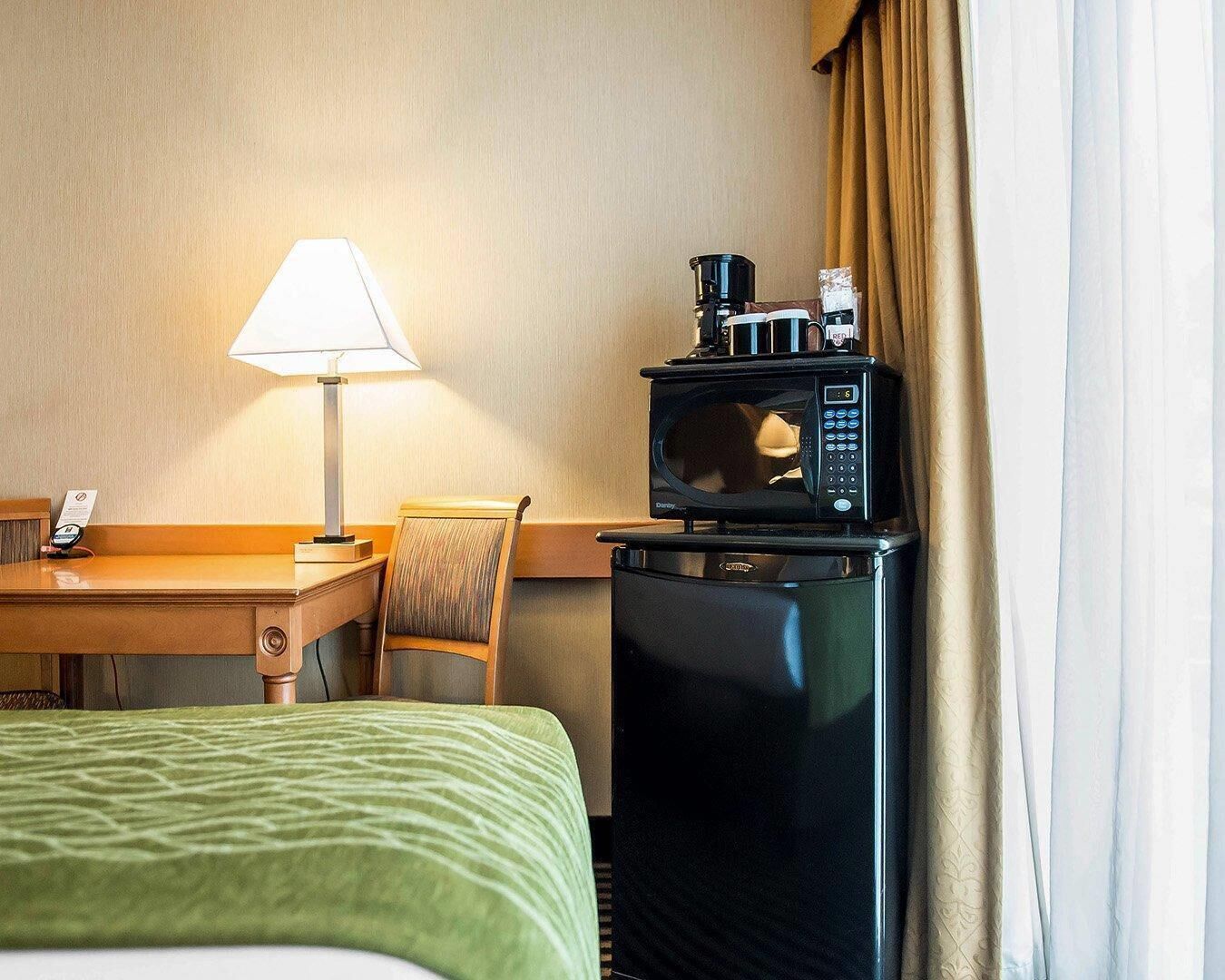 Una habitación de hotel con una cama, un escritorio con lámpara, un microondas y una silla.
