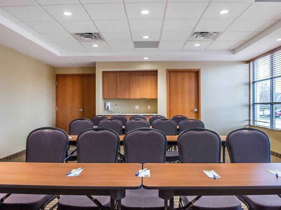 Un salón de conferencias con varias mesas y sillas, armarios de madera y un ventanal con persianas.