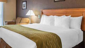 A hotel room with a large bed, a wooden headboard, a chair, a lamp, and two framed pictures on the wall.