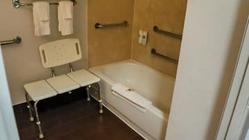A bathroom with a white bathtub, a white bench, and a white chair. There are two towel racks on the wall and a handrail on the bathtub.
