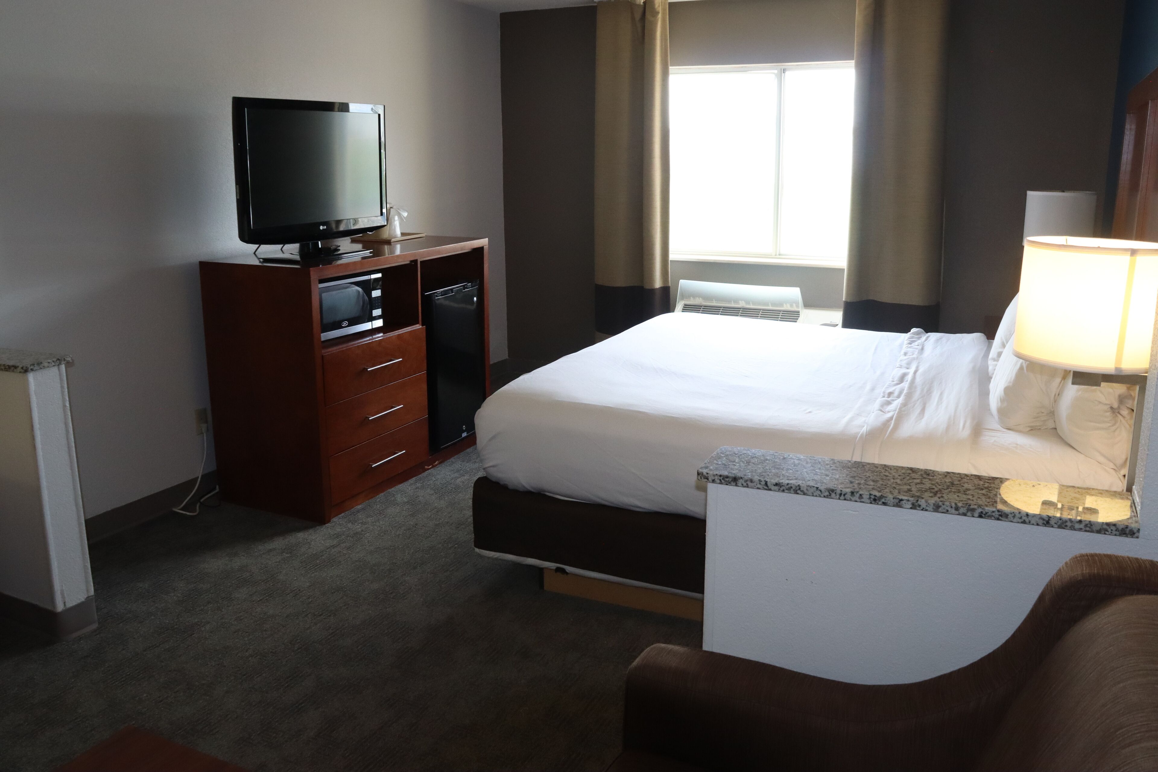Een hotelkamer met een bed, een televisie op een houten kast, een bureau met een lamp, en een raam met gordijnen.