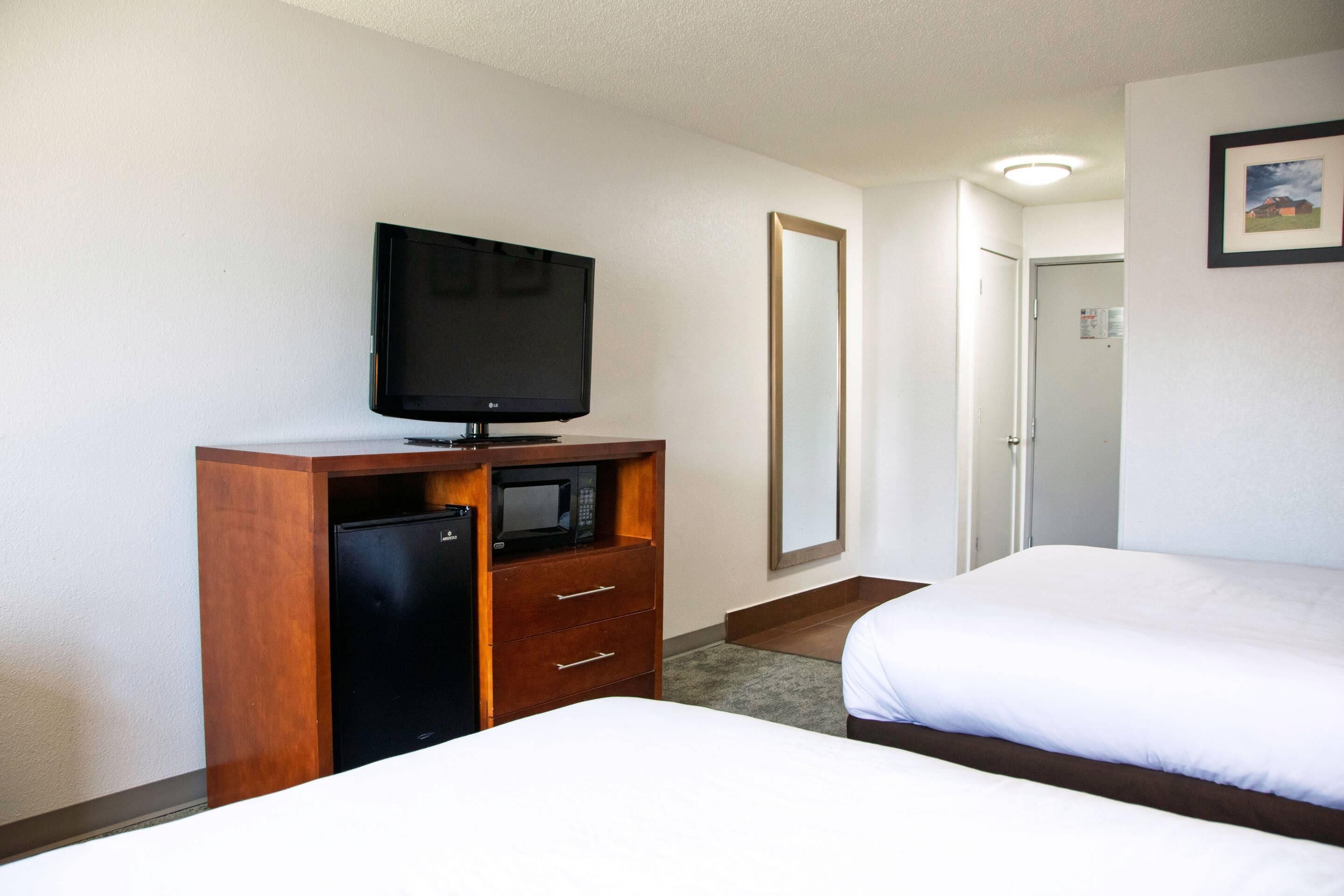 A hotel room with a TV, a microwave, a wooden dresser, two beds, and a door leading to another room.