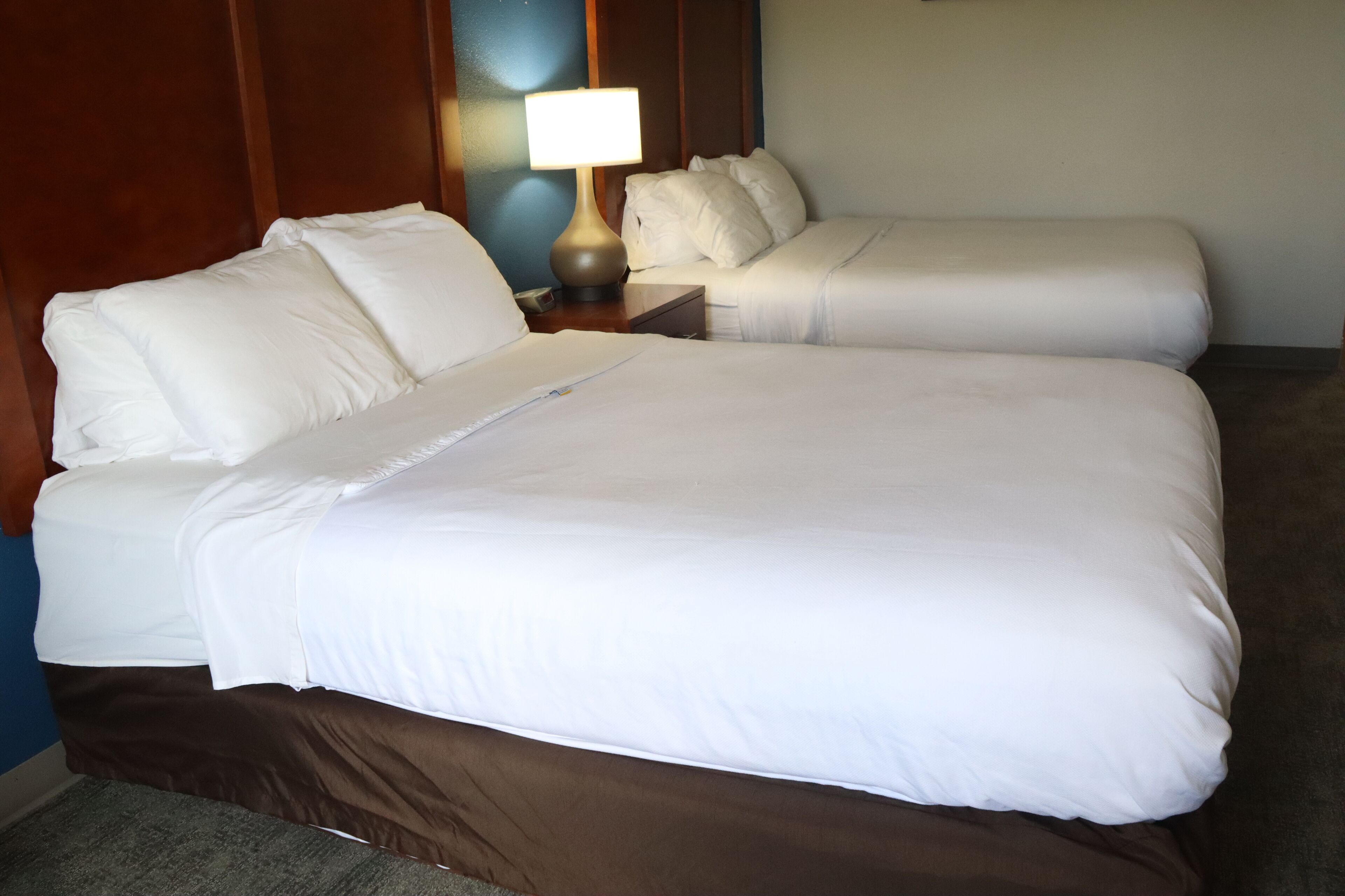 A hotel room with two beds, a nightstand with a lamp, and a wooden headboard.