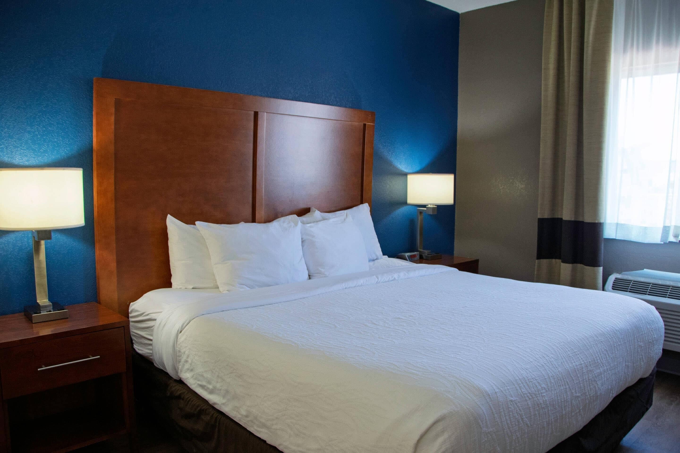 A neatly made bed with white linens, a wooden headboard, and two bedside lamps.