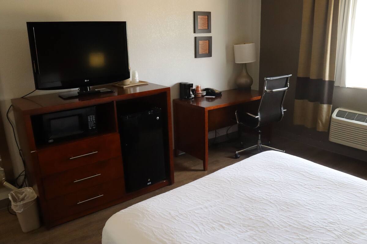 A hotel room with a bed, a desk with a computer, a television, a microwave, and a chair.