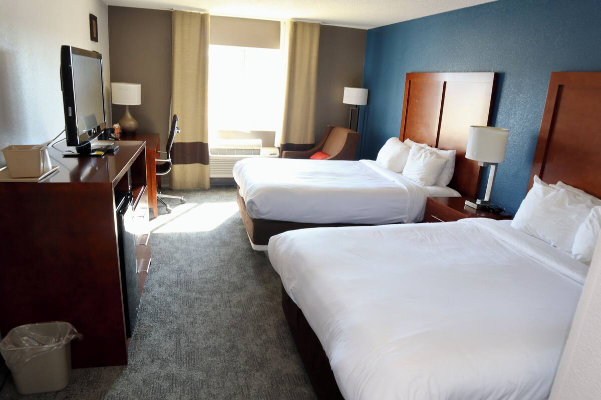 A hotel room with two beds, a desk with a computer, a chair, and a trash bin.