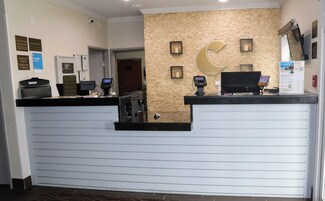 Una recepción con diseño moderno, con un fondo de pared de piedra y una decoración con forma de luna creciente. Hay varios letreros y un monitor de computadora en el mostrador.