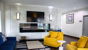 A modern living room with a stone wall, a flat-screen TV, a fireplace, and yellow and blue sofas. - Comfort Inn & Suites Coralville - Iowa City near Iowa River Landing (Coralville)