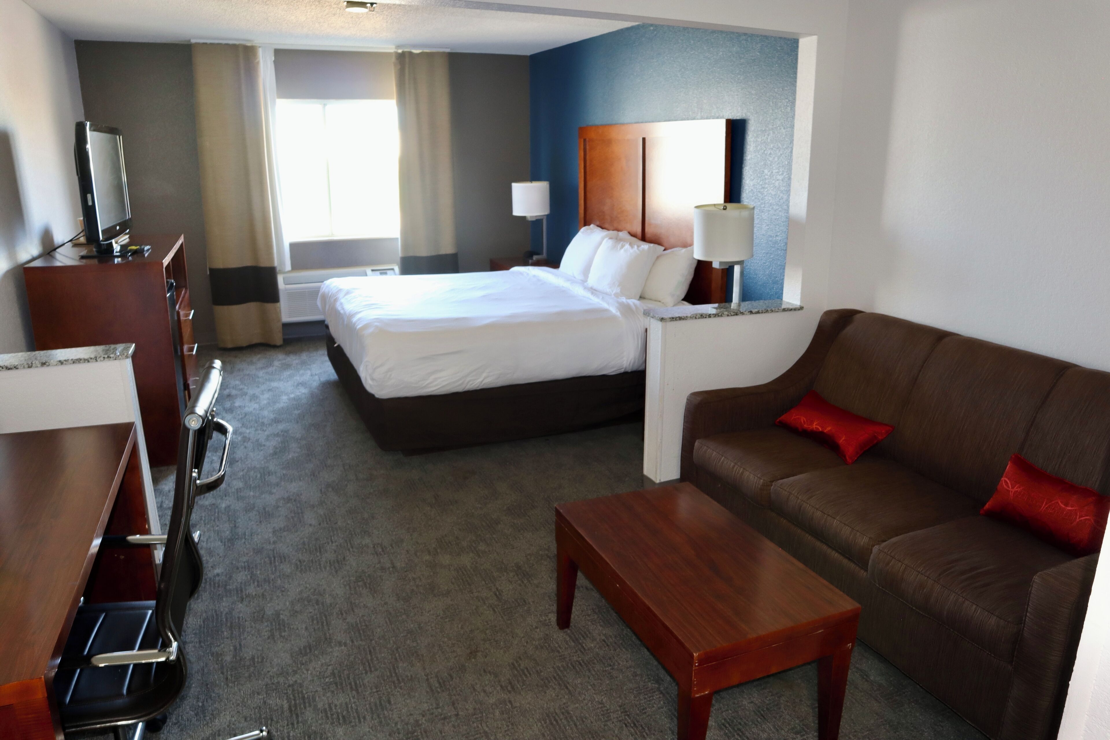 A hotel room with a bed, a sofa, a desk, and a TV.