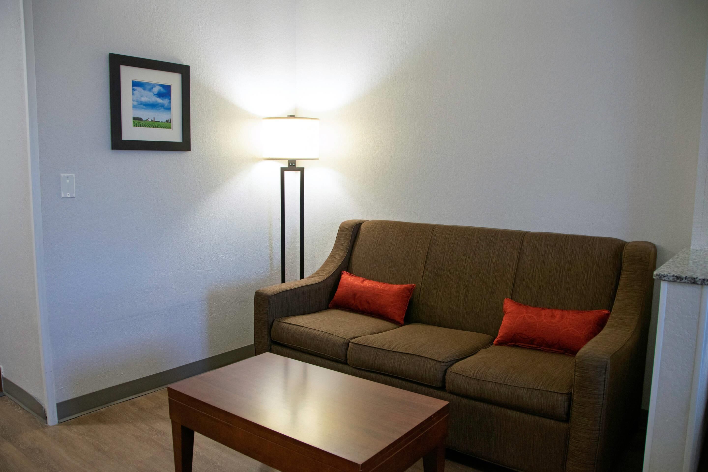 Ein Wohnzimmer mit einem braunen Sofa, zwei roten Kissen, einem Holztisch und einer Stehlampe.