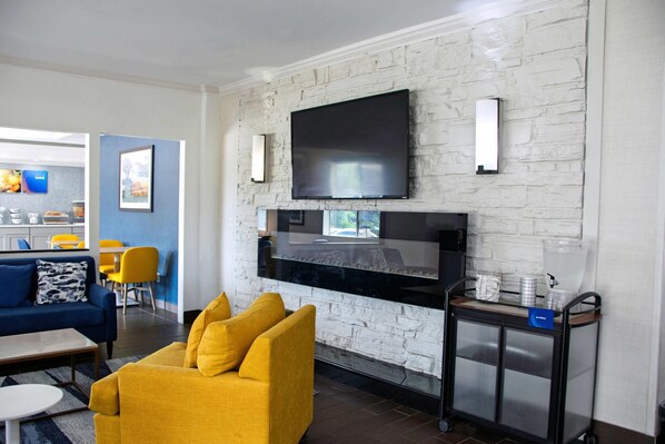 Una sala de estar moderna con un televisor de pantalla plana grande montado en una pared de ladrillo blanco, un sofá amarillo, un sofá azul y una mesita pequeña.