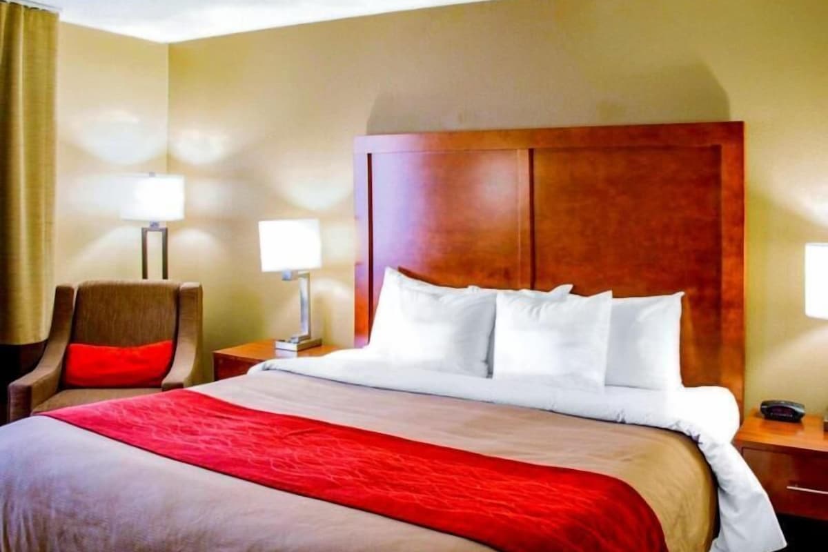 A hotel room with a large bed, a wooden headboard, two bedside tables with lamps, and a chair.