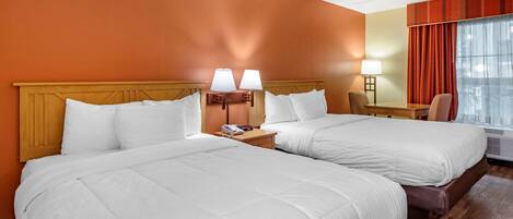 Una habitación de hotel con dos camas, un escritorio, una silla y una ventana con cortinas.