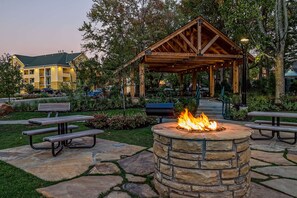 Un hogar de piedra con bancos, un pabellón cubierto y un edificio al fondo.