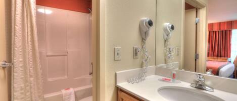 A bathroom with a white bathtub, a toilet, a sink with a mirror, and a hairdryer mounted on the wall.