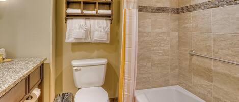A bathroom with a toilet, a sink, a trash bin, a shower curtain, and a bathtub.