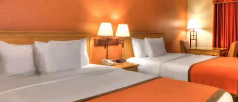 Habitación de hotel con dos camas, cada una con ropa blanca y un toque naranja. Hay dos lámparas de noche, una mesita de madera con un teléfono y una silla.