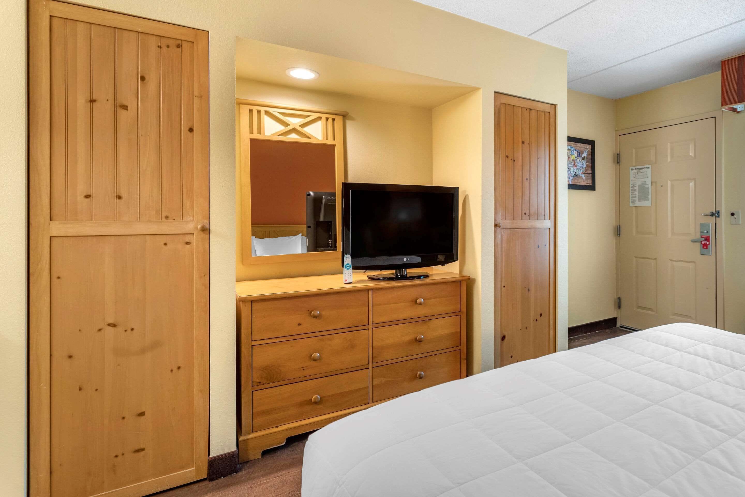 A hotel room with a bed, wooden wardrobe, a television on a dresser, and a mirror.
