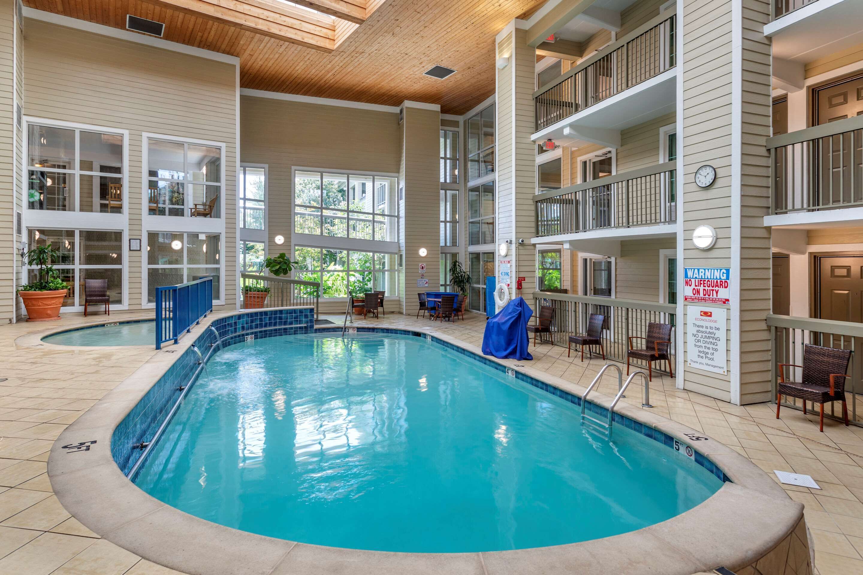 An indoor swimming pool with multiple levels of balconies, potted plants, and a sign warning about no lifeguard on duty.