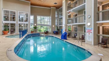 An indoor swimming pool with multiple levels of balconies, potted plants, and a sign warning about no lifeguard on duty.