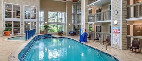 An indoor swimming pool with multiple levels of balconies, potted plants, and a sign warning about no lifeguard on duty.