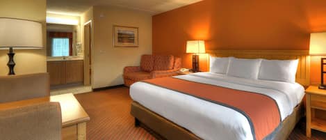 A hotel room with a large bed, a desk, a chair, and a bathroom visible through an open door.
