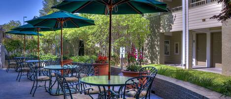 Outdoor patio seating with tables and chairs, green umbrellas, and potted plants.