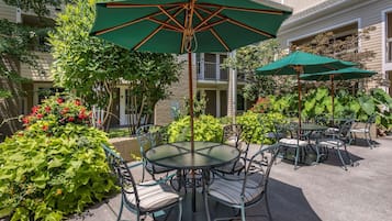 An outdoor patio with round tables and chairs, green umbrellas, and lush greenery.