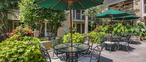 An outdoor patio with round tables and chairs, green umbrellas, and lush greenery.