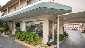 A hotel entrance with a covered walkway, a glass door, and a parking area. - El Camino Inn (Daly City)