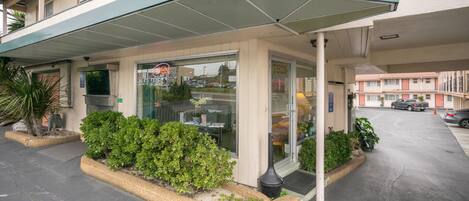 A hotel entrance with a covered walkway, a glass door, and a parking area.