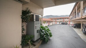 A parking area with a building in the background, a refrigerator, and some plants. - El Camino Inn (Daly City)