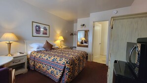 A hotel room with a bed, bedside lamps, a bedside table, a mirror, and a TV. - El Camino Inn (Daly City)