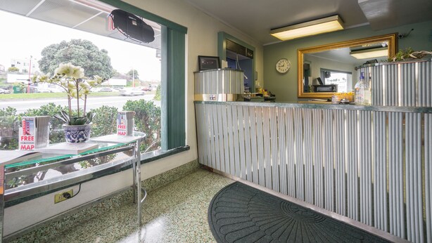 A reception area with a counter, a potted plant, a clock, and a mirror. - El Camino Inn (Daly City)