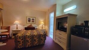 Ein Hotelzimmer mit einem Bett, zwei Nachttischlampen, einem Fernseher, einer Mikrowelle, einem kleinen Tisch und einem Stuhl.