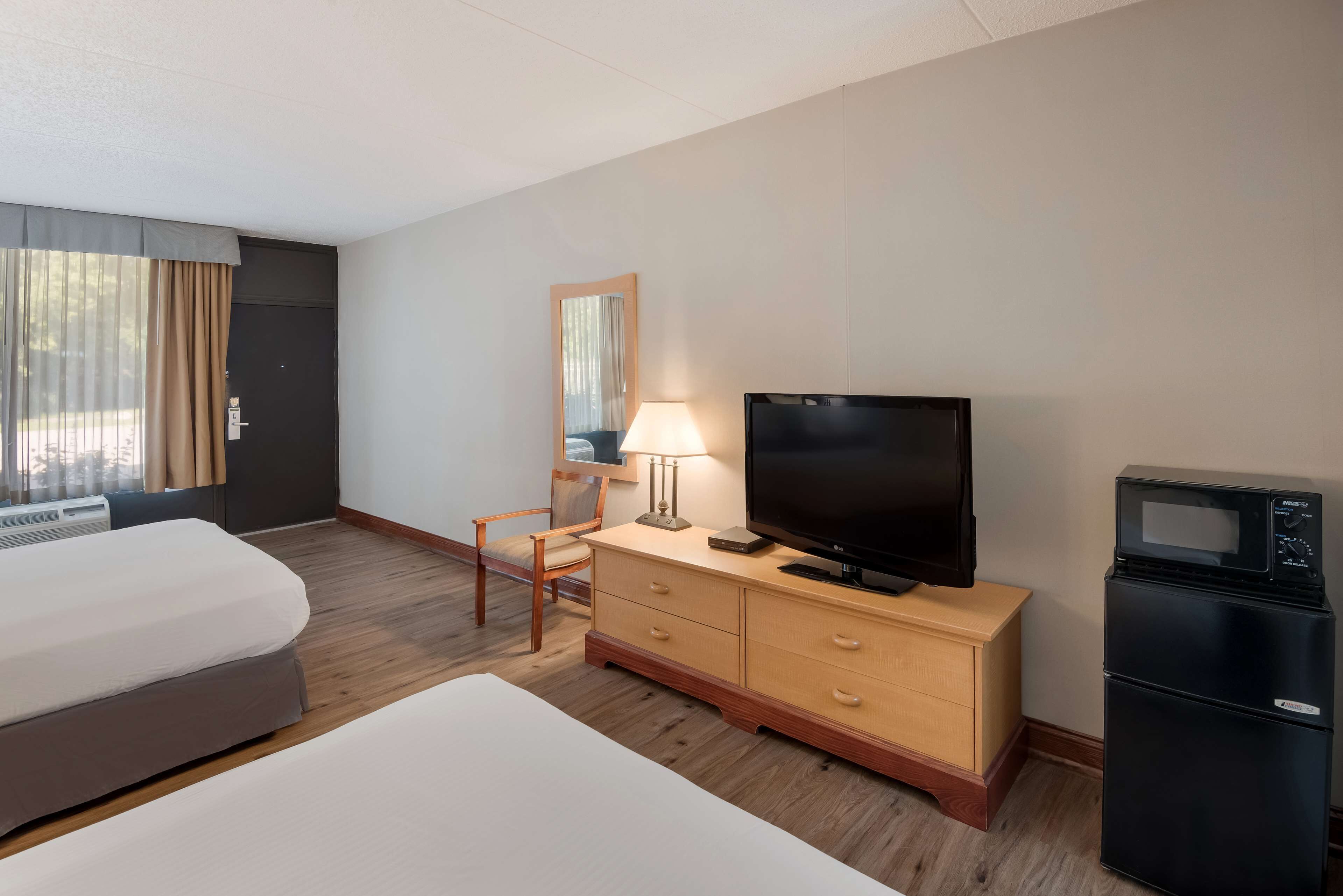 Een hotelkamer met een bed, een televisie, een dressoir, een stoel en een koelkast.