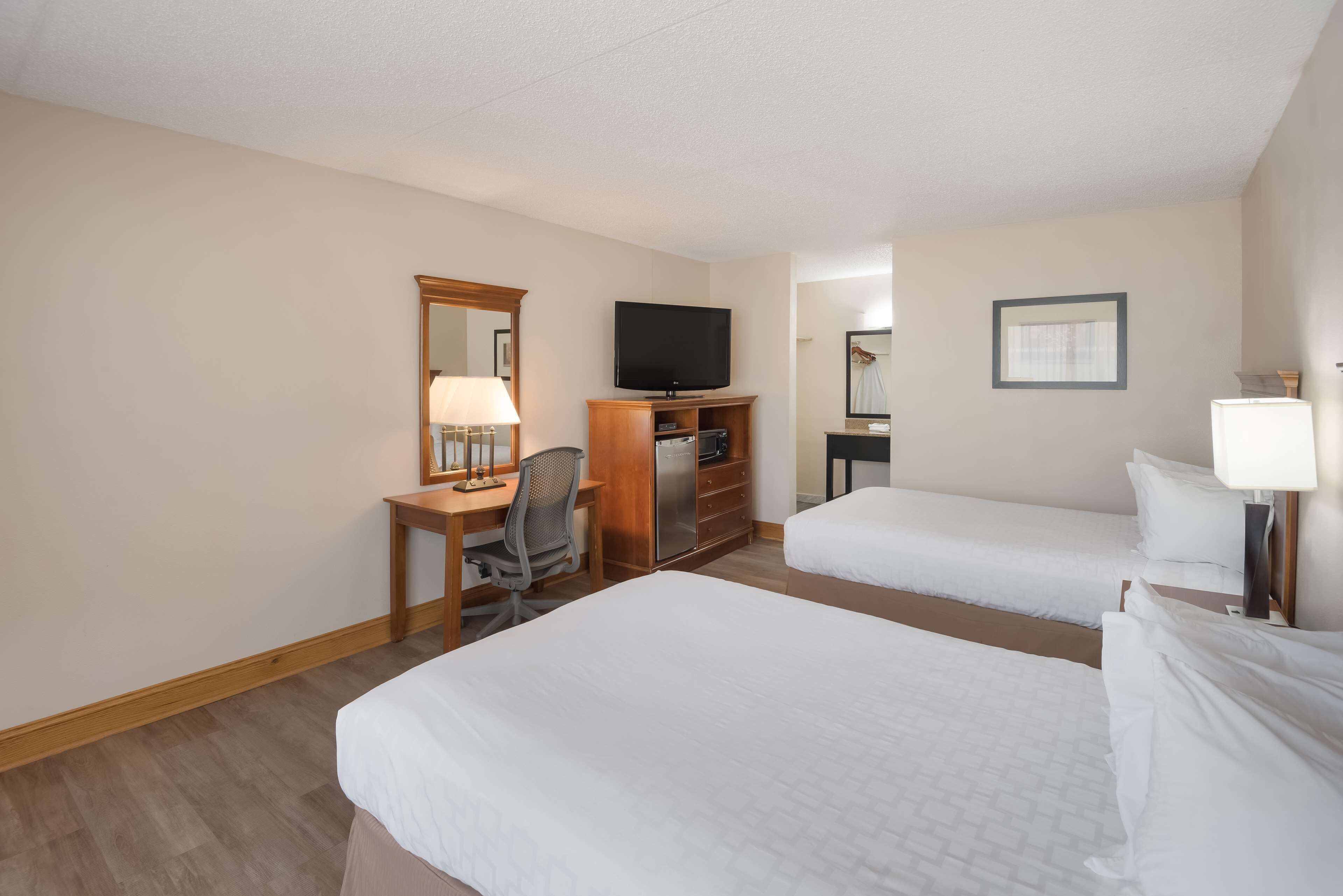 A hotel room with two single beds, a desk with a chair, a television, and a mirror.