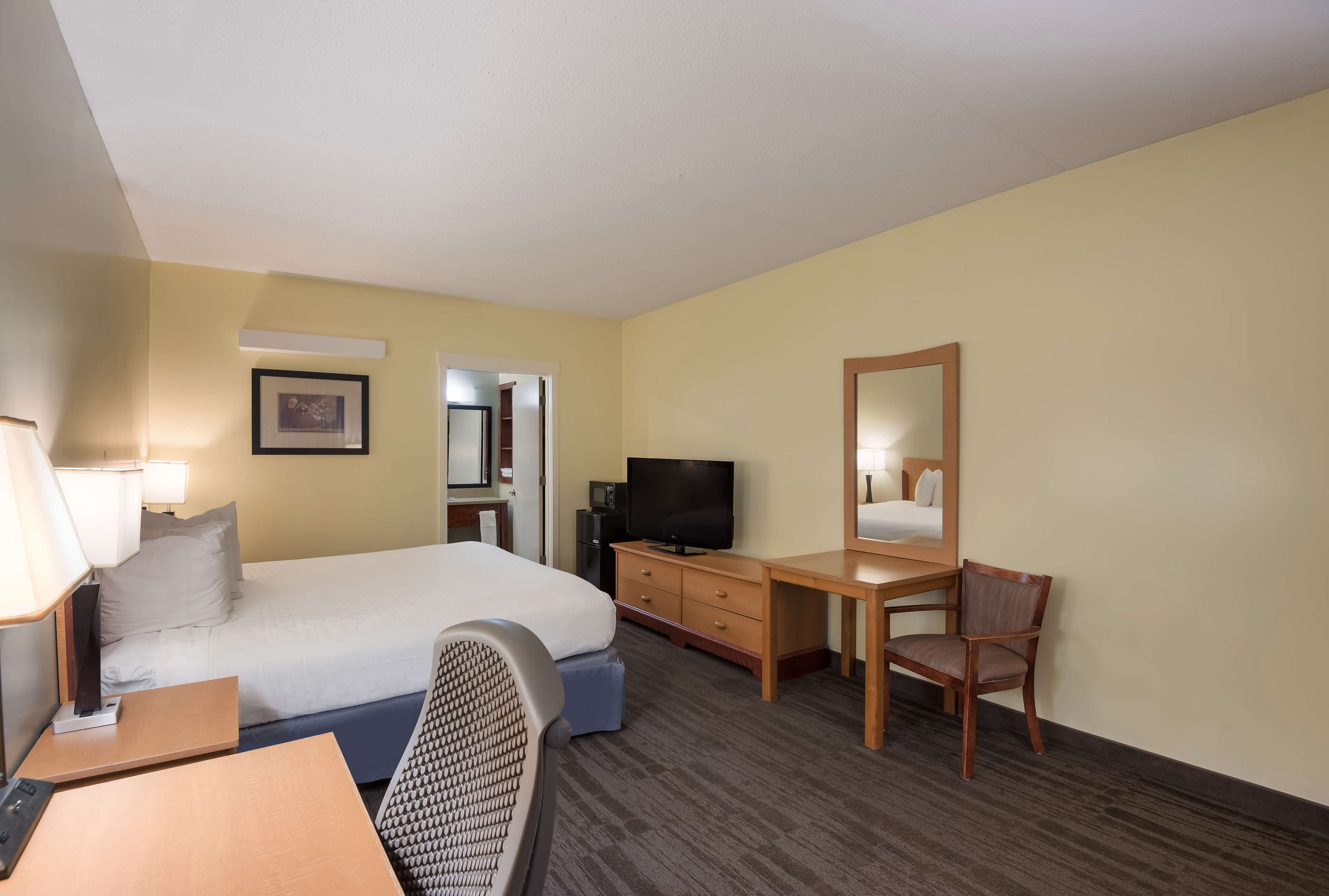A hotel room with a bed, a desk, a chair, a television, and a mirror.