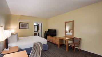 A hotel room with a bed, a desk, a chair, a television, and a mirror.
