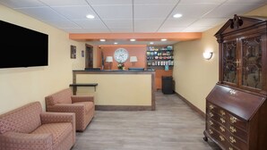 A reception area with a counter, two armchairs, a clock, a lamp, a cabinet, and a wall-mounted shelf with snacks. - Best Western Inn (Goshen)