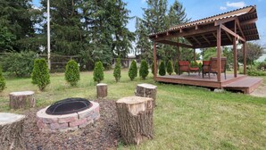 A wooden gazebo with a platform and seating, surrounded by a landscaped garden with trimmed bushes and a fire pit. - Best Western Inn (Goshen)
