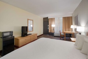A hotel room with a bed, a desk, a chair, a television, a microwave, and a dresser.