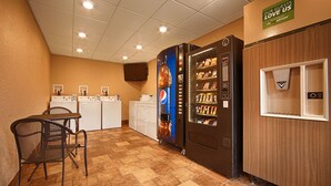 A laundry room with a vending machine, a table with chairs, and a refrigerator. - Best Western Inn (Goshen)