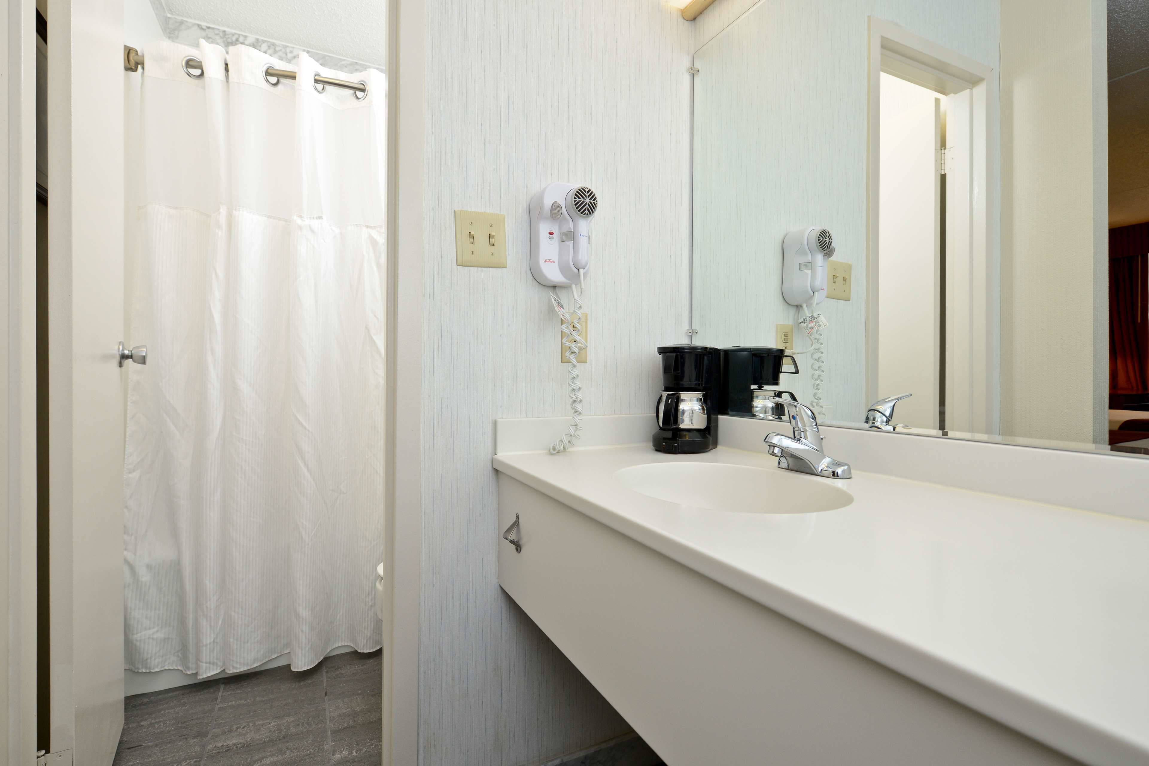 A bathroom with a white sink, a mirror, a hairdryer, and a shower curtain.